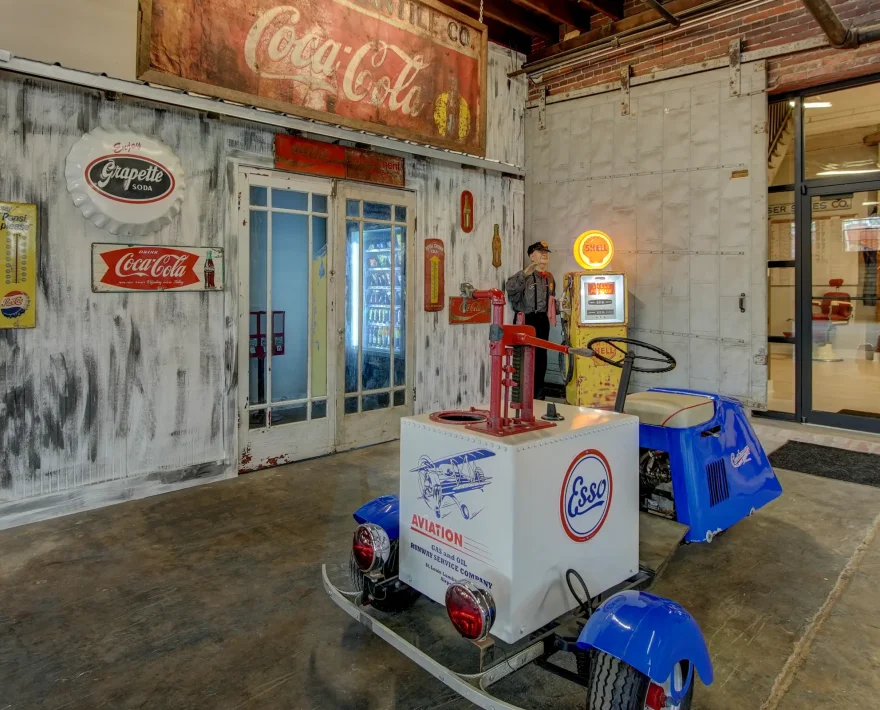 Ground-level common area at Lofts at Creek Street with restored vintage Coca-Cola signage, retro vending display, and historic gas-station decor