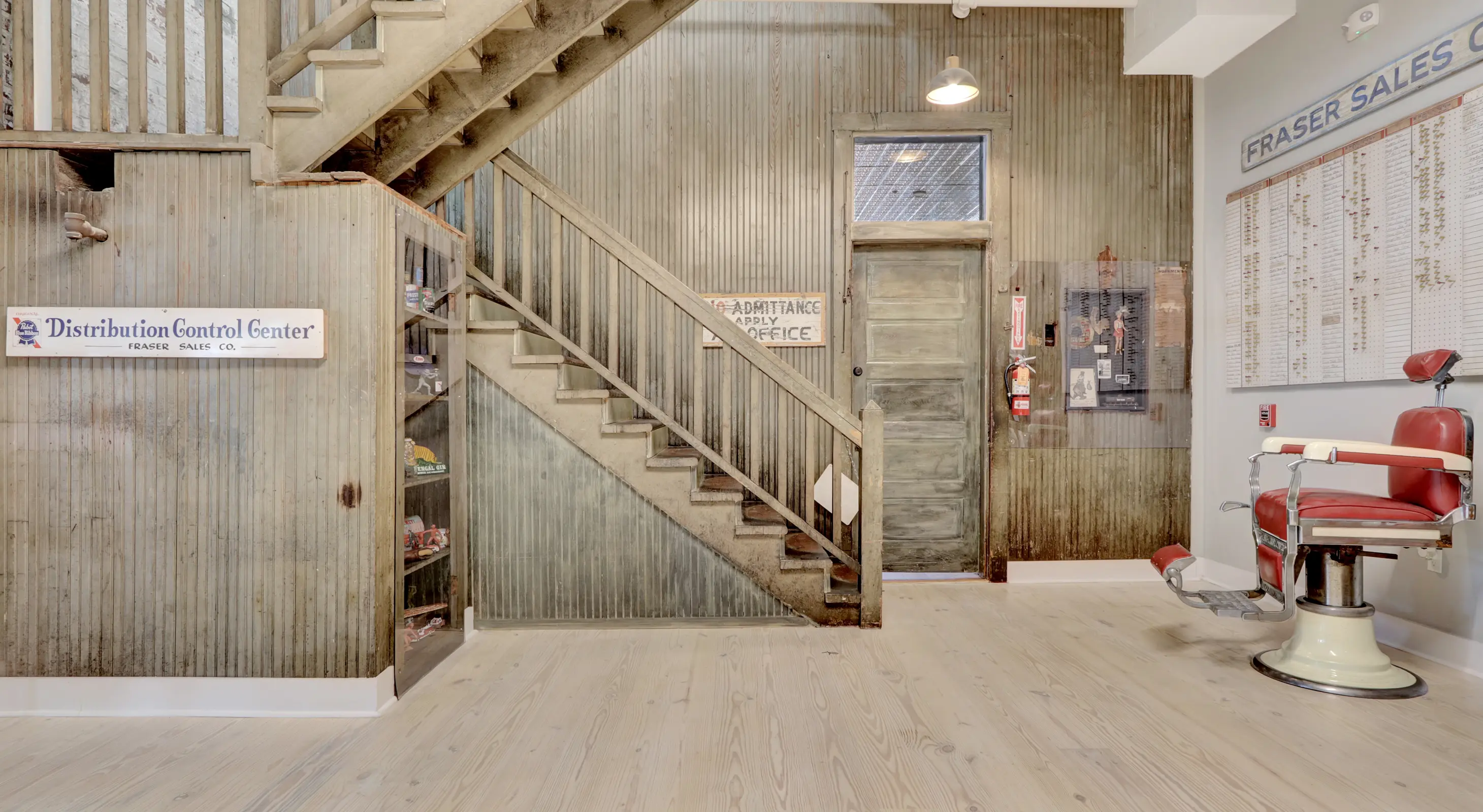 Interior foyer of Lofts at Creek Street with restored wooden staircase, corrugated metal walls, and vintage Fraser Sales Co. signage.