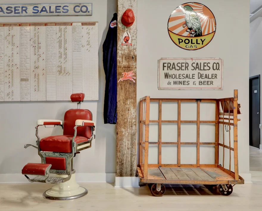 Restored common area at Lofts at Creek Street featuring a vintage barber chair, Fraser Sales Co. signs, and preserved industrial architectural elements