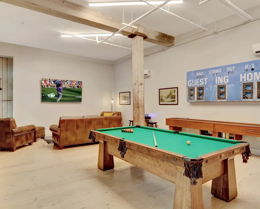 Guest game room in a renovated historic accommodation, featuring a pool table, leather lounge seating, and vintage sports-inspired décor