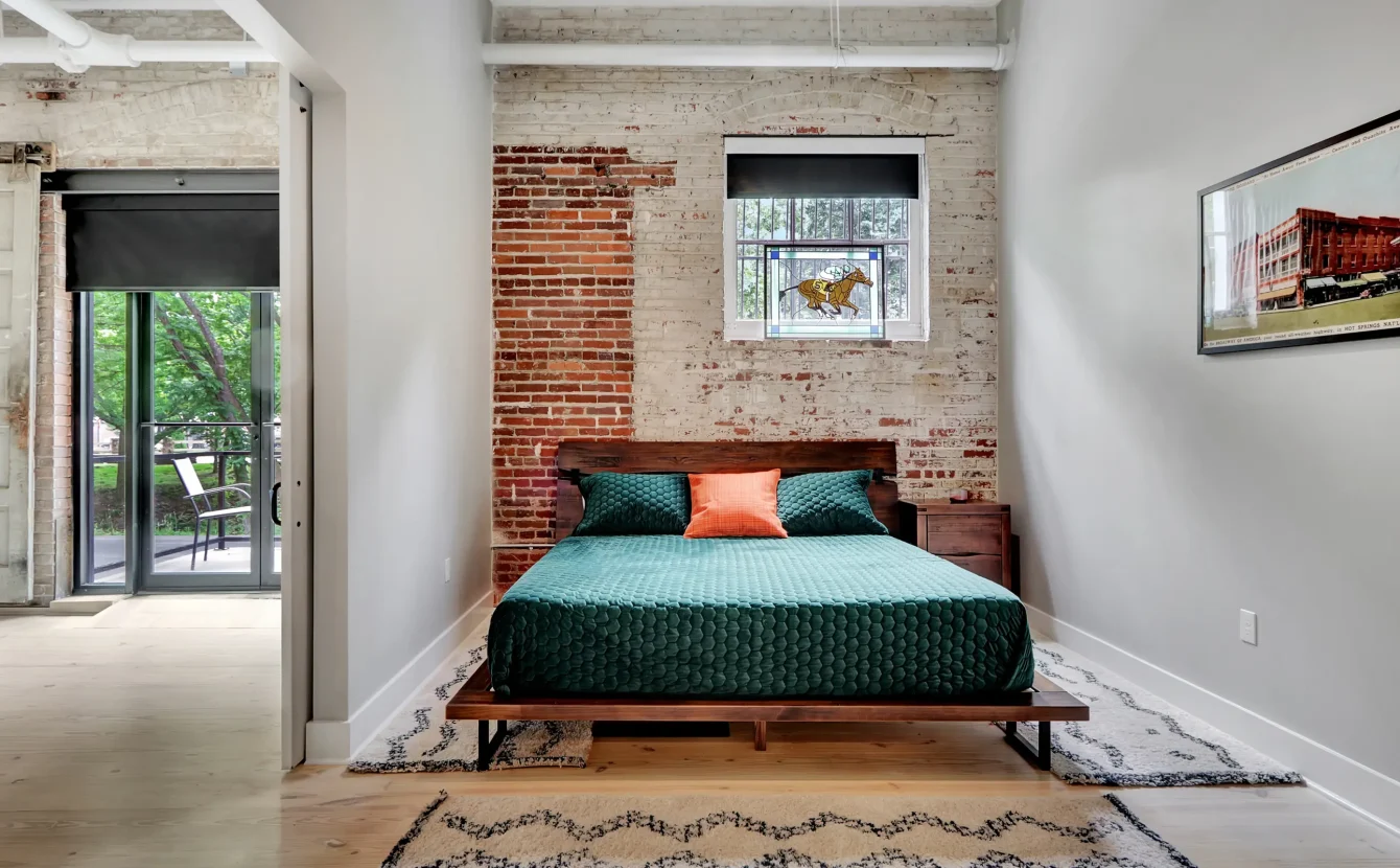 Loft-style bedroom in a Hot Springs rental with brick accents and sliding doors opening to the main living space