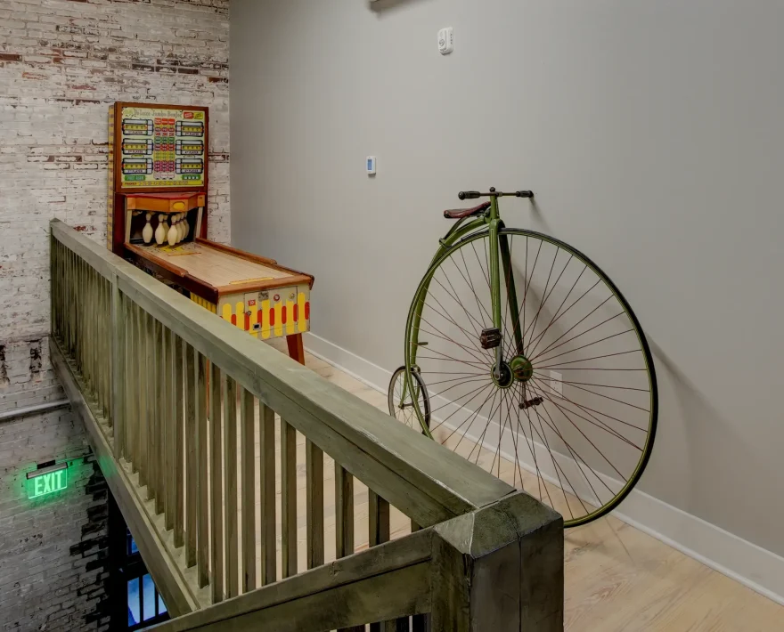 Upper landing in a historic brick building showcasing an antique high-wheel bicycle and a vintage bowling arcade game