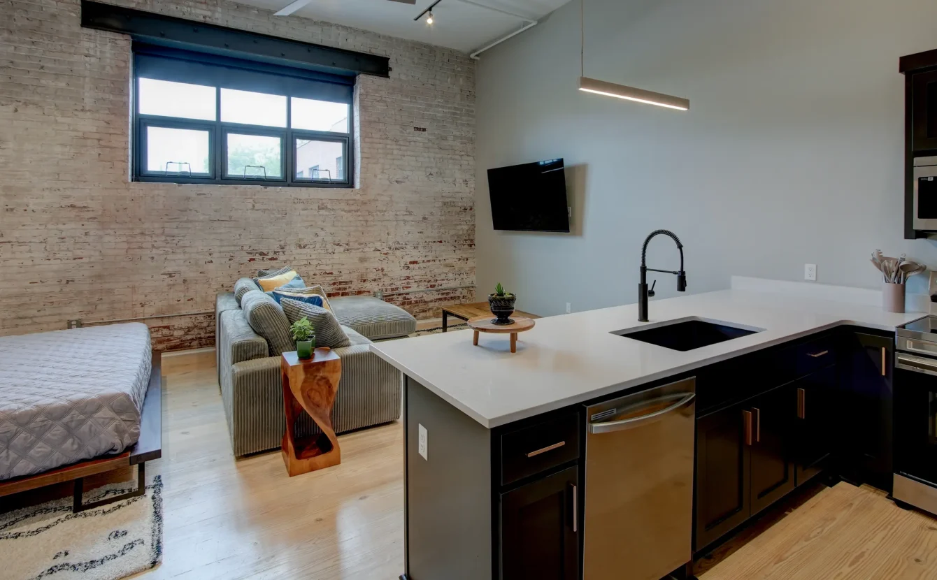 Living area inside The Como accommodation featuring exposed brick, a mounted TV, and contemporary seating