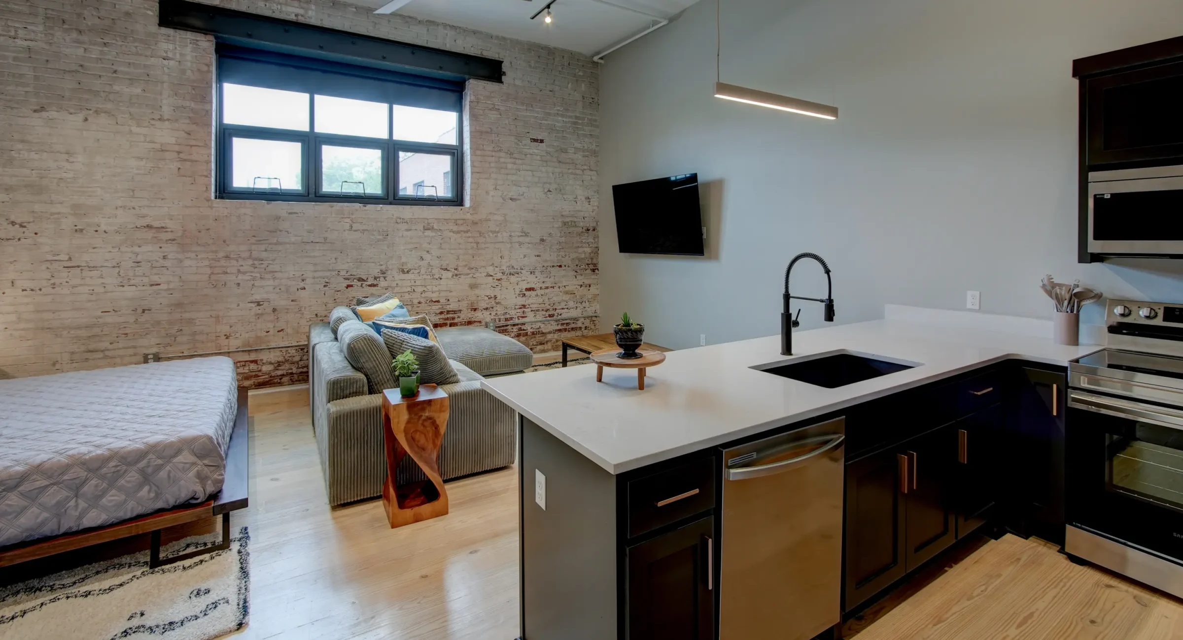 Living area inside The Como accommodation featuring exposed brick, a mounted TV, and contemporary seating