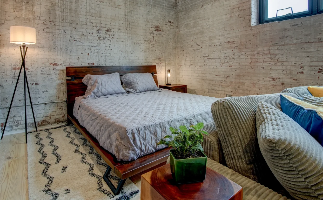 Sleeping area in The Como accommodation with exposed brick walls and a contemporary wood platform bed