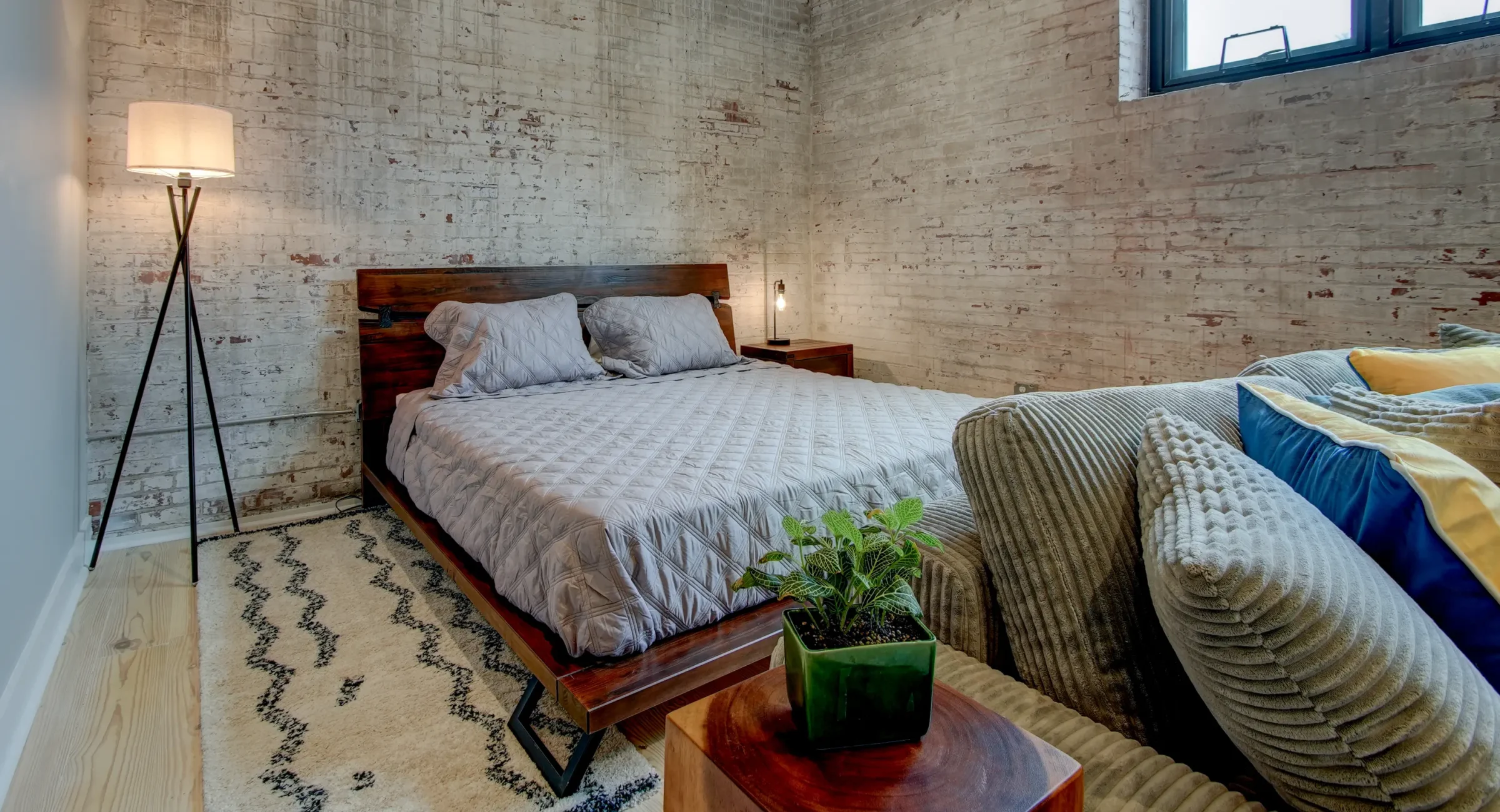 Sleeping area in The Como accommodation with exposed brick walls and a contemporary wood platform bed