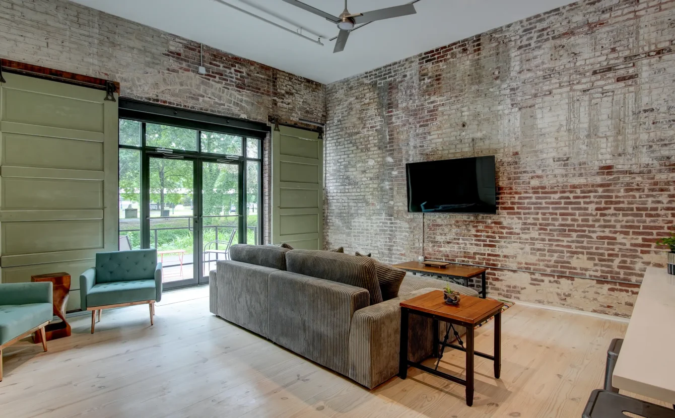 Loft-style living room in a downtown Hot Springs rental with exposed brick, oversized windows, and comfortable seating