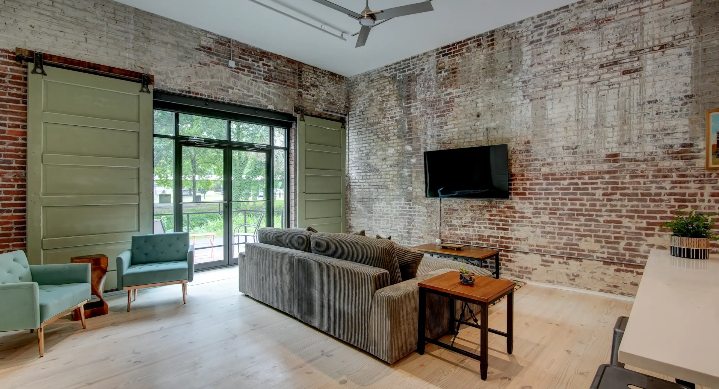 Loft-style living room in a downtown Hot Springs rental with exposed brick, oversized windows, and comfortable seating