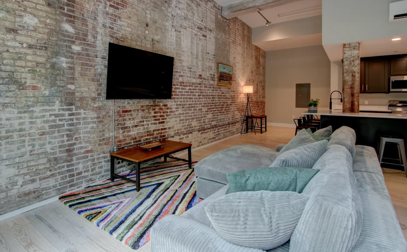 Cozy living area in a renovated Hot Springs loft featuring exposed brick, a mounted TV, and modern furnishings