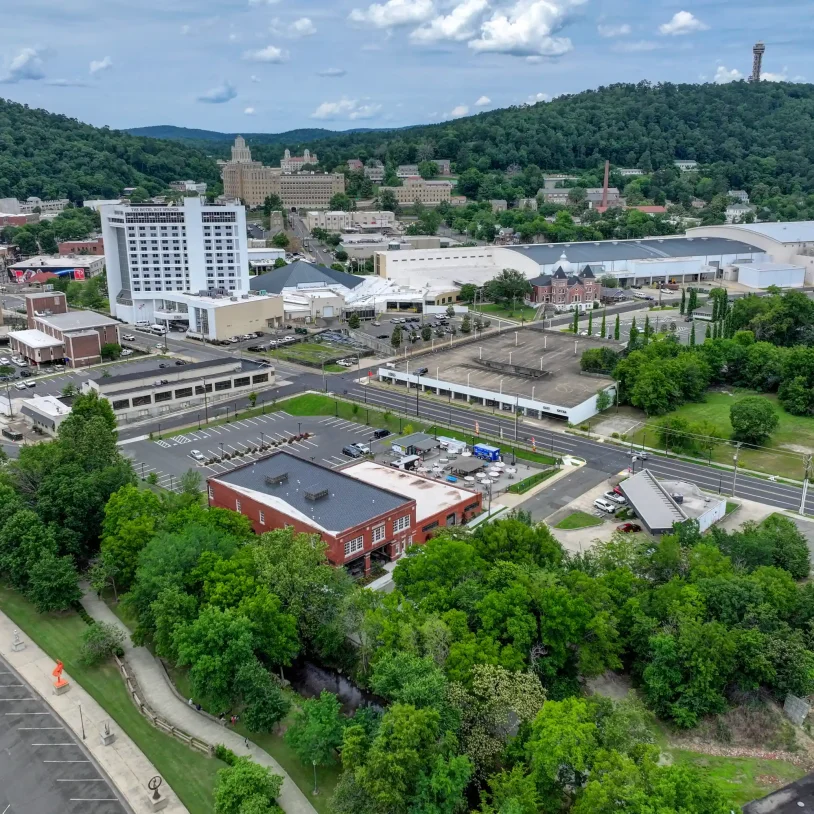 Aerial shot of the historic brick property bordered by creekside trees, with downtown Hot Springs, AR hotels and historic bathhouse buildings in the distance