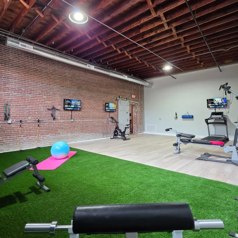 Fitness room combining exposed brick architecture with modern exercise equipment, turf flooring, and resistance training stations