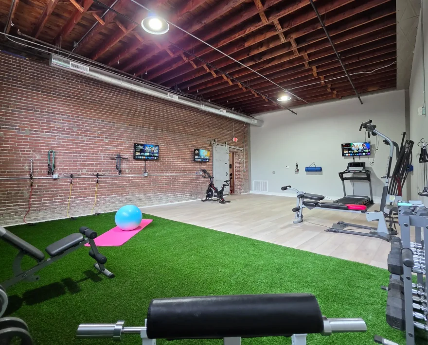 Fitness room combining exposed brick architecture with modern exercise equipment, turf flooring, and resistance training stations