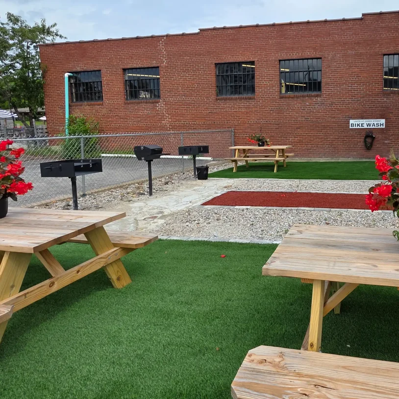 Guest courtyard featuring picnic tables, charcoal grills, and landscaped turf pathways next to the historic brick property