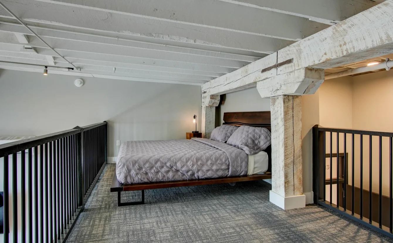 Loft bedroom with brick wall and wood beam ceiling at Lofts at Creek Street