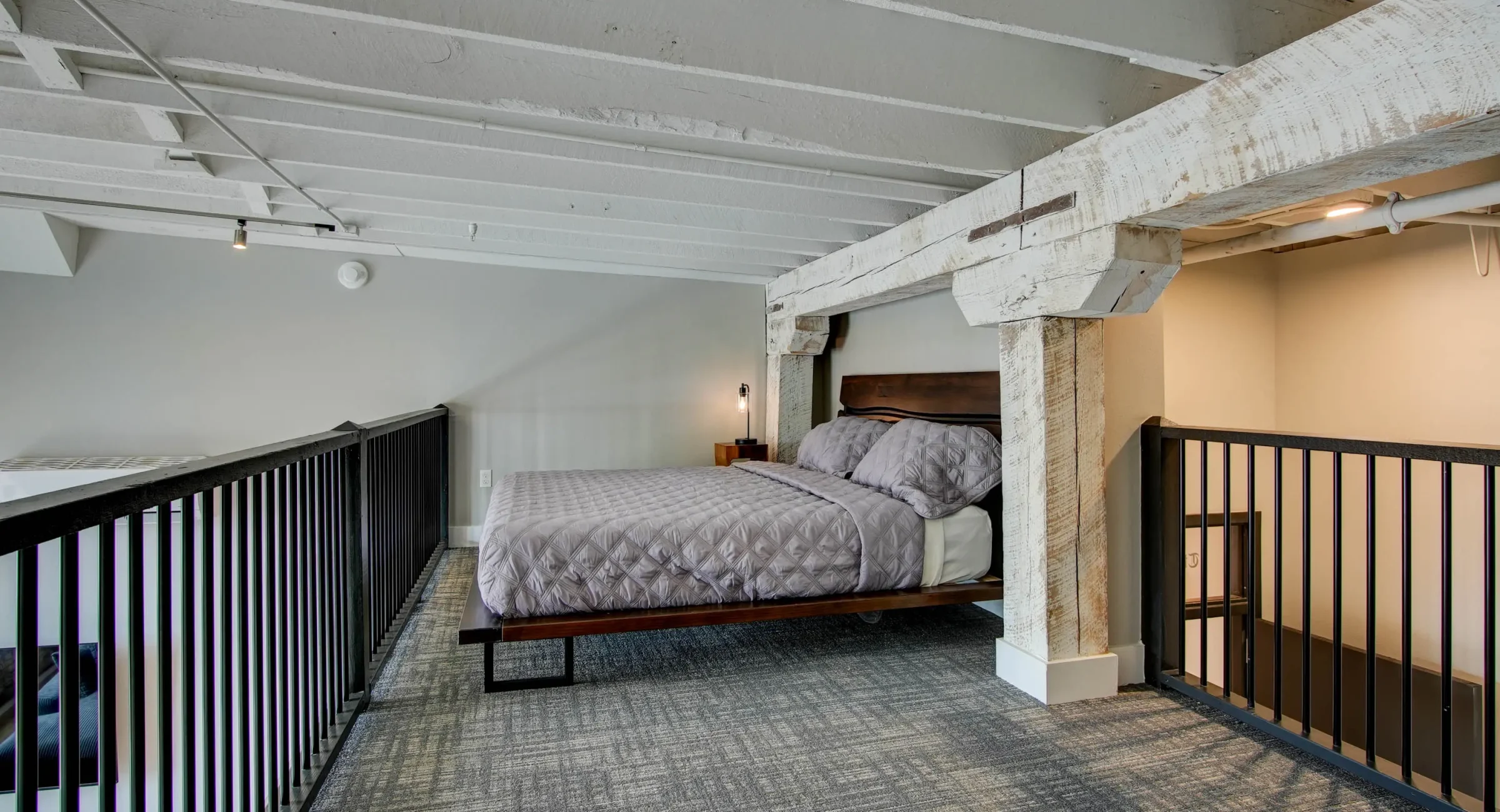 Loft bedroom with brick wall and wood beam ceiling at Lofts at Creek Street